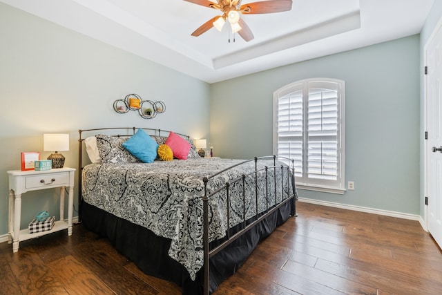 bedroom with ceiling fan, baseboards, a tray ceiling, and hardwood / wood-style flooring