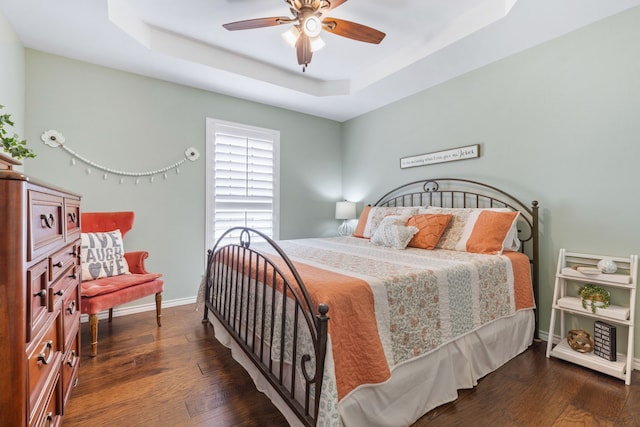 bedroom featuring ceiling fan, baseboards, dark wood-type flooring, and a tray ceiling