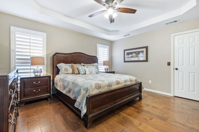 bedroom featuring a tray ceiling, visible vents, baseboards, and dark wood-type flooring