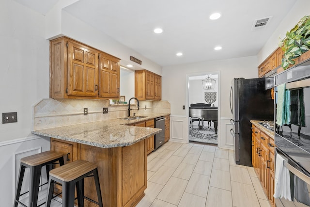 kitchen featuring light stone countertops, a kitchen bar, a peninsula, stainless steel appliances, and a sink