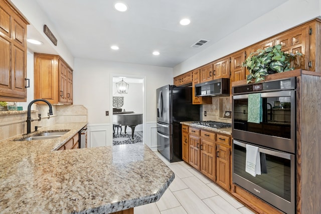 kitchen featuring visible vents, light stone counters, wainscoting, stainless steel appliances, and a sink