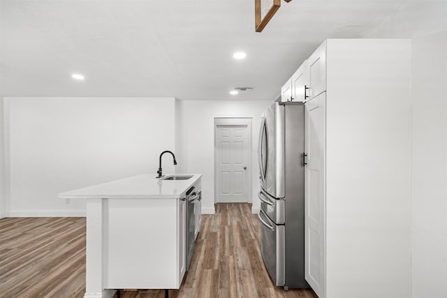 kitchen with visible vents, an island with sink, light wood-style flooring, stainless steel appliances, and a sink