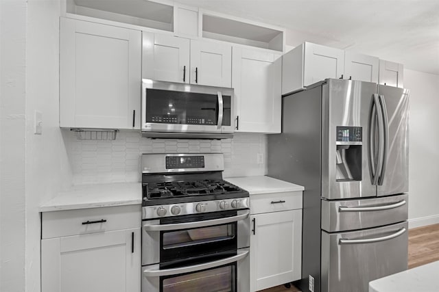 kitchen featuring wood finished floors, light stone countertops, decorative backsplash, white cabinets, and appliances with stainless steel finishes