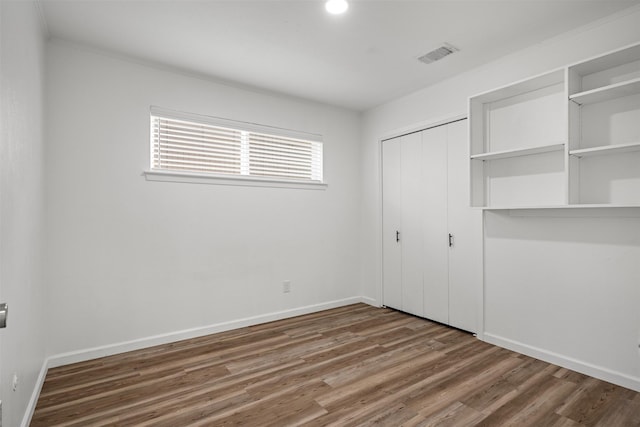 unfurnished bedroom featuring wood finished floors, visible vents, a closet, and baseboards