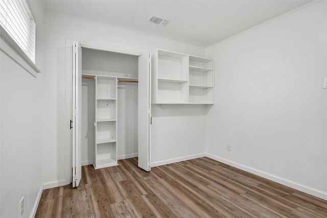 unfurnished bedroom with visible vents, ornamental molding, wood finished floors, a closet, and baseboards