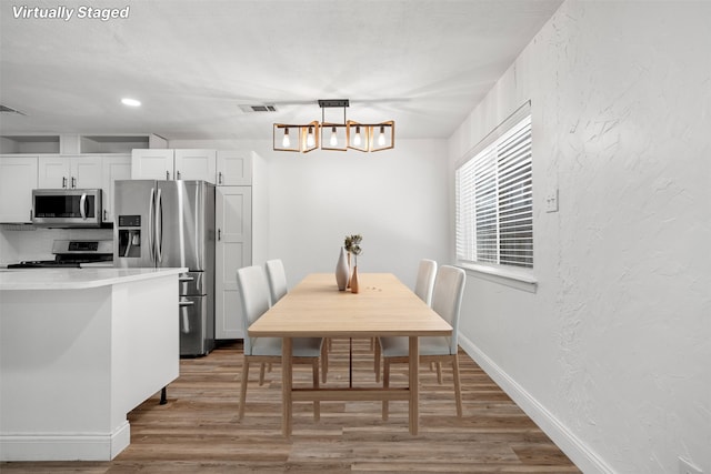 dining area featuring light wood finished floors, visible vents, baseboards, and a textured wall