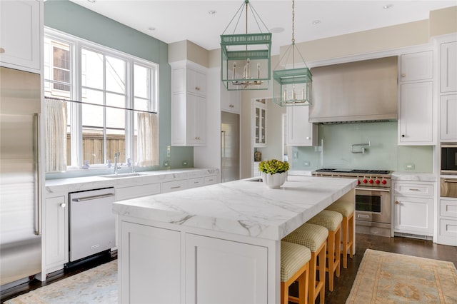 kitchen with a center island, built in appliances, custom range hood, white cabinetry, and a sink