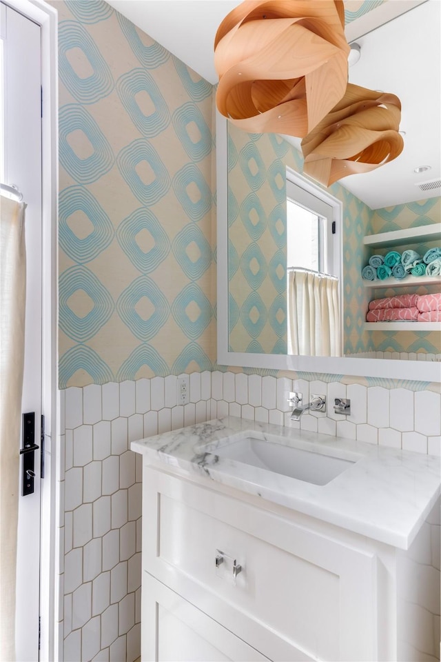 bathroom with visible vents, tile walls, vanity, and wallpapered walls