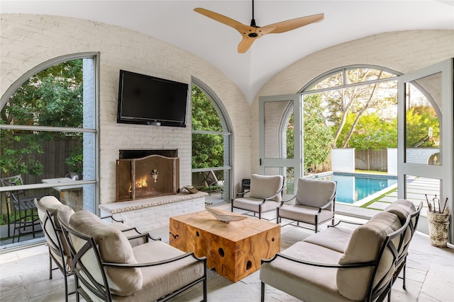 interior space with vaulted ceiling, a brick fireplace, a ceiling fan, and stone tile floors