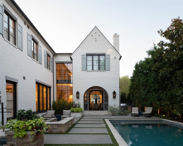 back of house featuring an outdoor pool, a patio, and brick siding