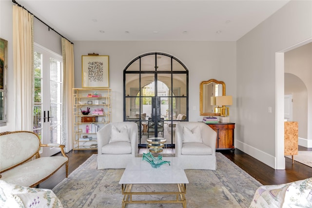 living area with wood finished floors, french doors, arched walkways, and baseboards