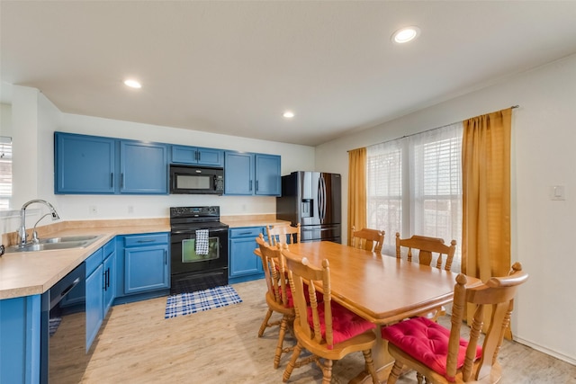 kitchen with light wood finished floors, a sink, black appliances, light countertops, and blue cabinets