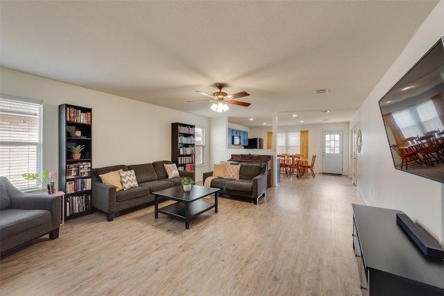 living room with visible vents, light wood-style flooring, and ceiling fan