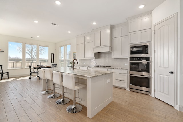 kitchen featuring light stone countertops, visible vents, light wood-style flooring, stainless steel appliances, and decorative backsplash