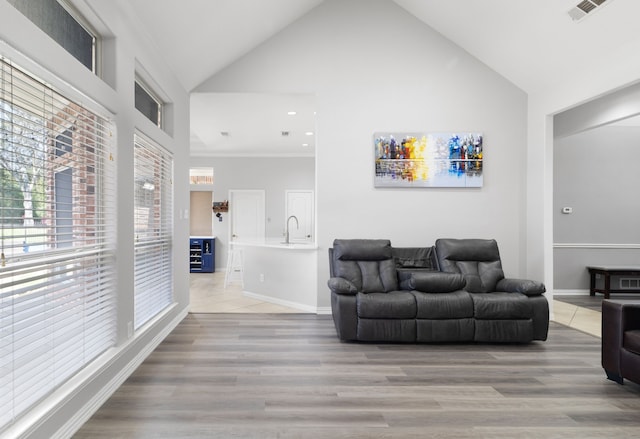 living area featuring baseboards, visible vents, light wood finished floors, and high vaulted ceiling