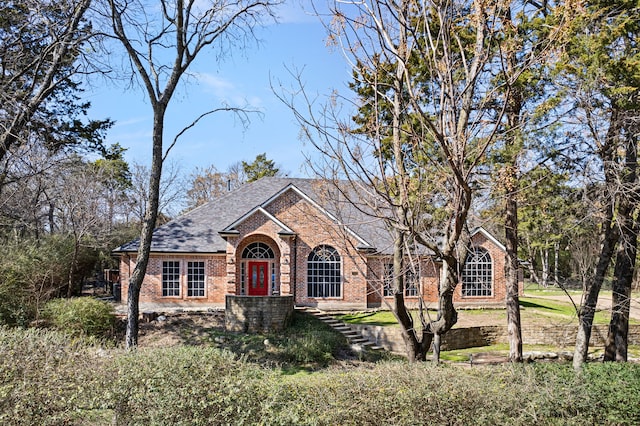 view of front of property featuring brick siding and roof with shingles