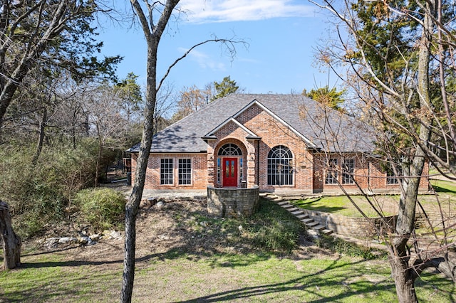 view of front of home featuring a front yard, brick siding, and a shingled roof