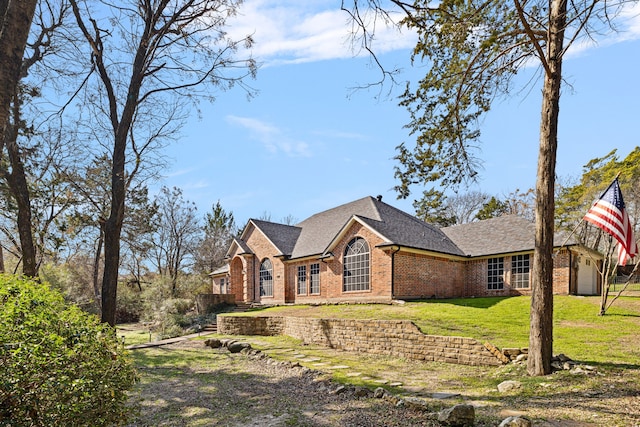 view of front of house with brick siding, a shingled roof, and a front yard