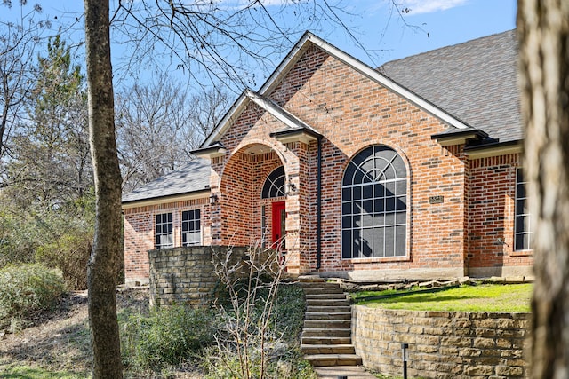 view of front of house with brick siding and roof with shingles