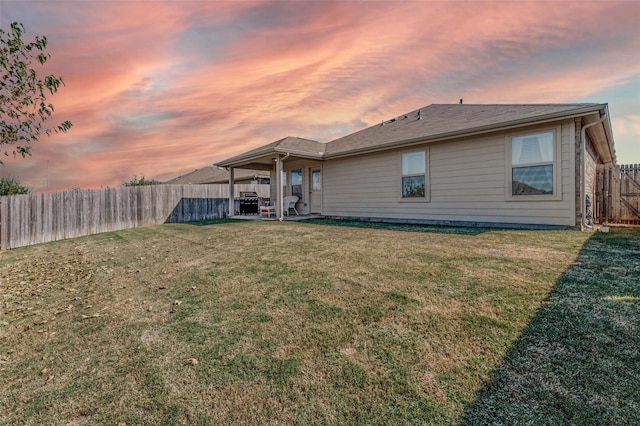 back of property at dusk featuring a lawn, a fenced backyard, and a patio area