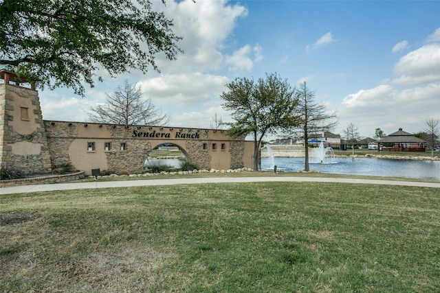 community / neighborhood sign featuring a lawn and a water view