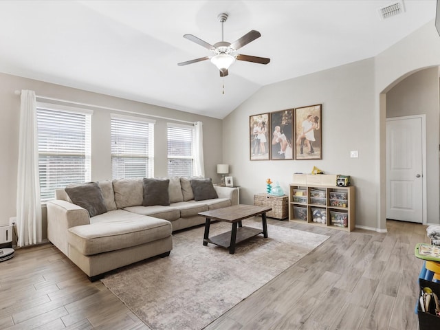 living room with a ceiling fan, visible vents, arched walkways, vaulted ceiling, and light wood-style floors