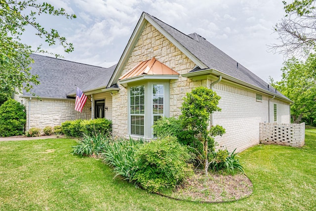 view of side of home featuring metal roof, stone siding, a lawn, and a shingled roof