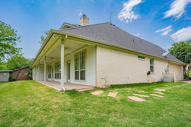 rear view of house with a ceiling fan, a chimney, a lawn, a patio area, and brick siding