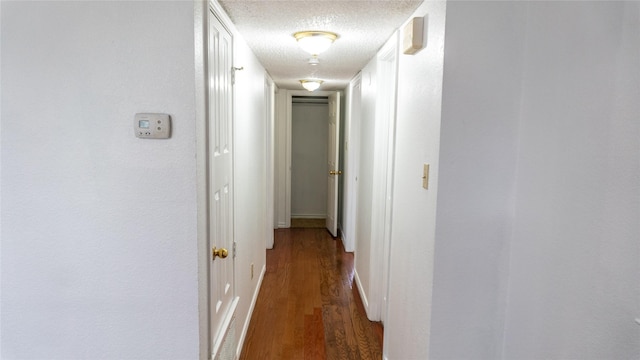 hallway featuring wood finished floors, baseboards, and a textured ceiling