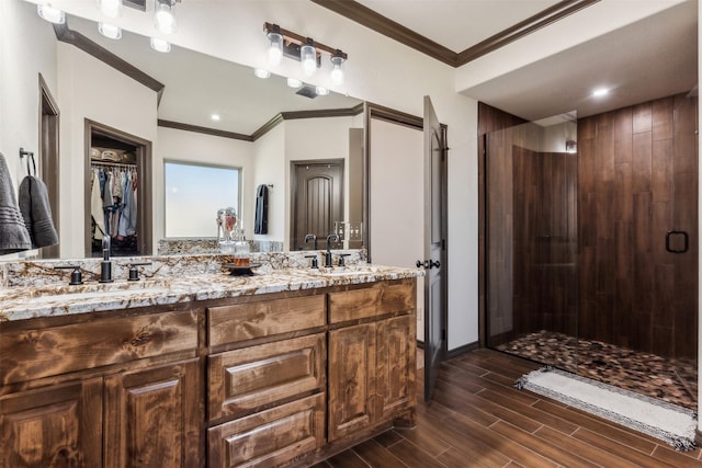 bathroom with wood finish floors, ornamental molding, a shower stall, and a sink