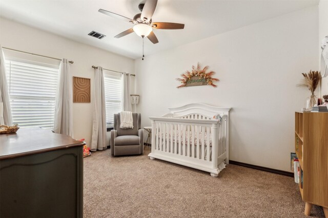 bedroom featuring visible vents, baseboards, light carpet, a nursery area, and a ceiling fan