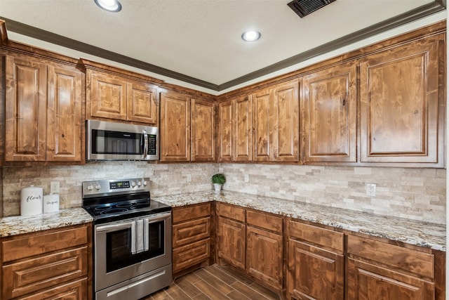 kitchen with light stone countertops, visible vents, wood finish floors, stainless steel appliances, and backsplash