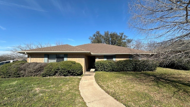 view of front of house with a front yard, brick siding, and a shingled roof