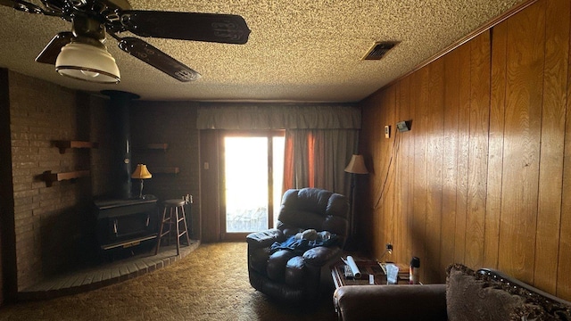 living room featuring visible vents, carpet, wood walls, a wood stove, and a textured ceiling