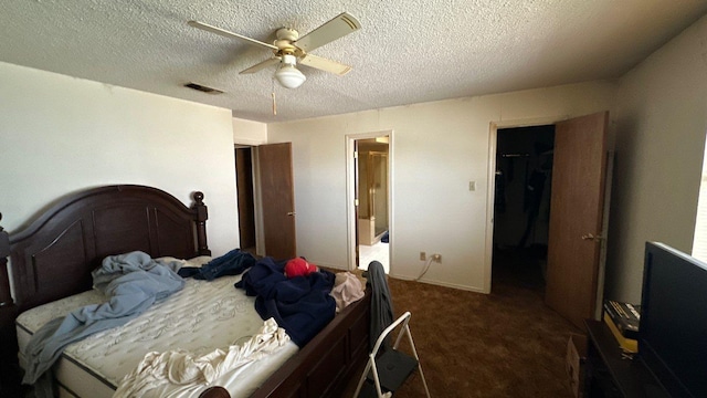 bedroom featuring a ceiling fan, visible vents, a spacious closet, a textured ceiling, and dark colored carpet