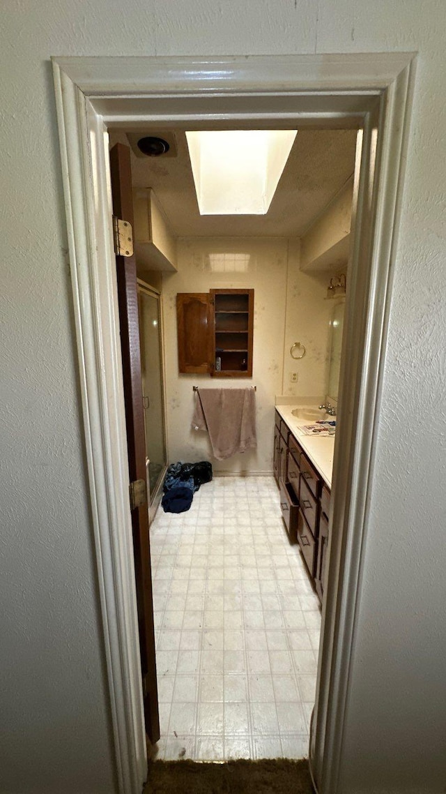 full bathroom featuring tile patterned floors, a skylight, a shower stall, vanity, and a textured wall