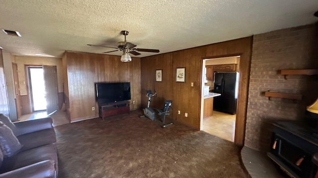 unfurnished living room featuring visible vents, a textured ceiling, wooden walls, ceiling fan, and a wood stove