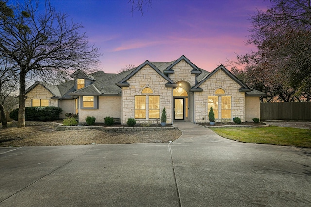 french provincial home featuring a shingled roof and fence