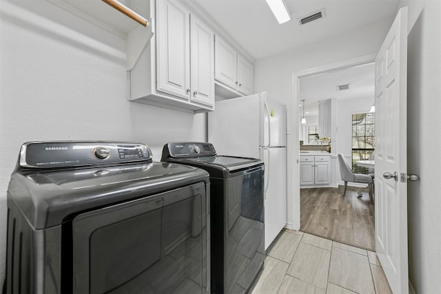 washroom featuring light wood-style floors, cabinet space, washing machine and dryer, and visible vents