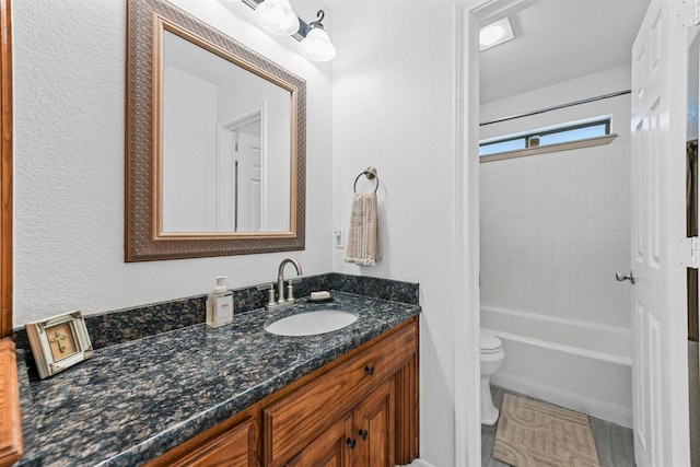 bathroom with shower / bath combination, toilet, vanity, and a textured wall