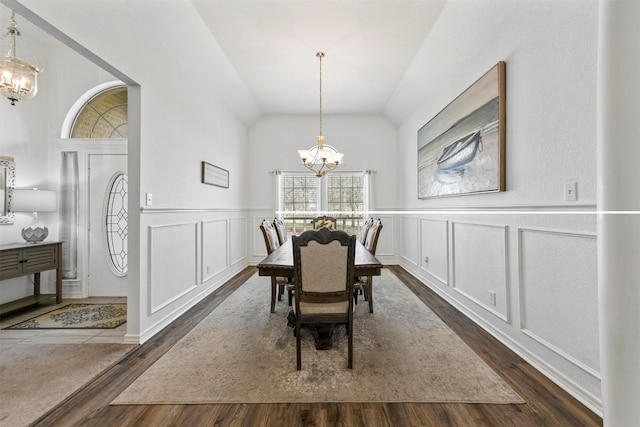 dining room with a notable chandelier, vaulted ceiling, dark wood-style flooring, and a decorative wall