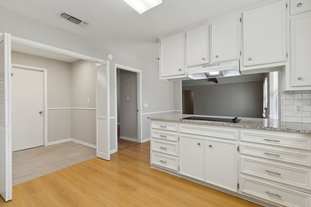 kitchen featuring visible vents, under cabinet range hood, tasteful backsplash, white cabinetry, and light wood finished floors