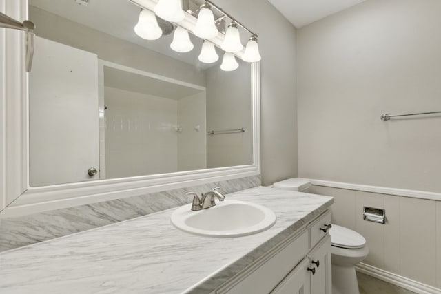 bathroom with a wainscoted wall, toilet, and vanity