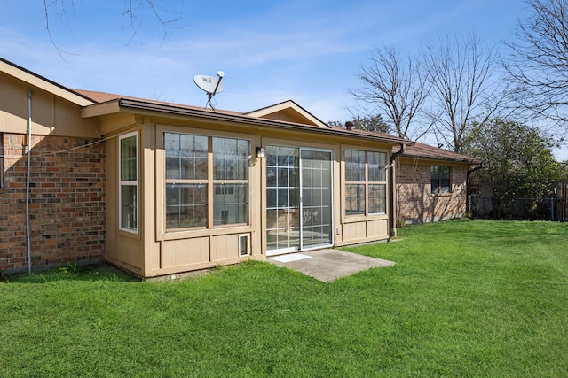 rear view of property featuring brick siding, a lawn, and fence