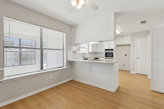 kitchen featuring visible vents, a peninsula, white cabinets, light wood finished floors, and stainless steel oven