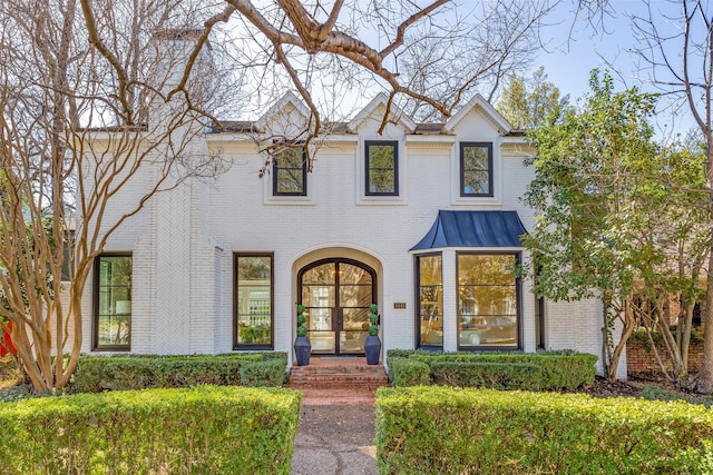 modern farmhouse style home with a standing seam roof, french doors, brick siding, and metal roof