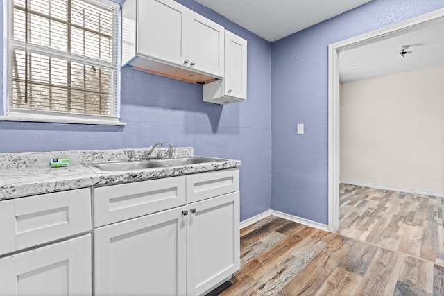 kitchen with baseboards, light wood-style flooring, a sink, light countertops, and white cabinets