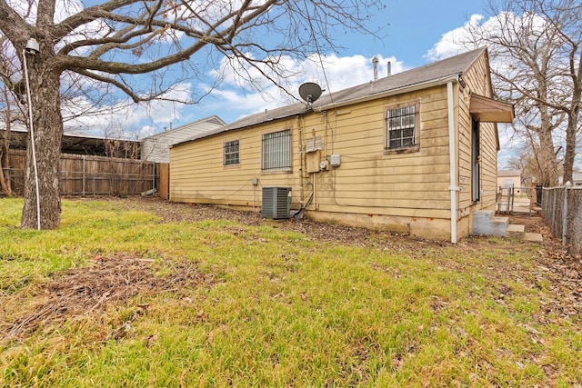 rear view of house with a yard, central AC unit, and a fenced backyard