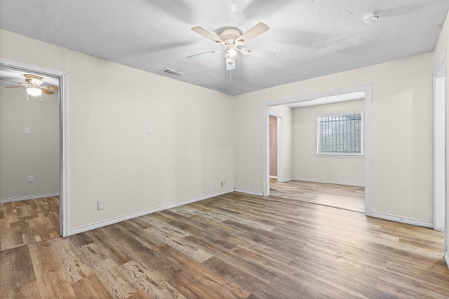 spare room with a ceiling fan, wood finished floors, visible vents, and baseboards