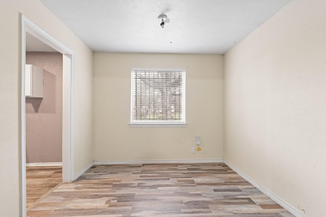 spare room with baseboards and wood finished floors